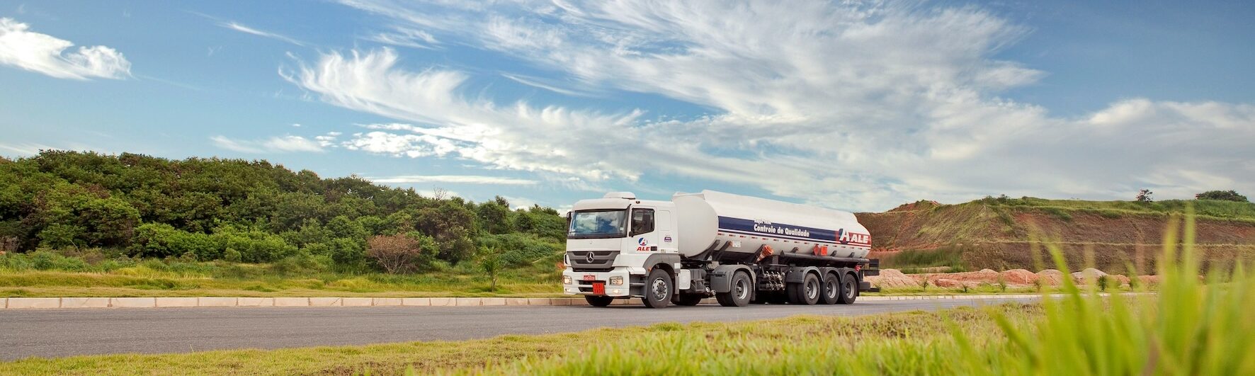 Ein LKW fährt durch eine weite, grüne Landschaft, mit leichten Hügeln.