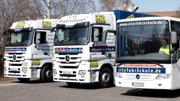In einer Reihe stehen zwei LKW und ein Bus der Cityfahrschule nebeneinander.