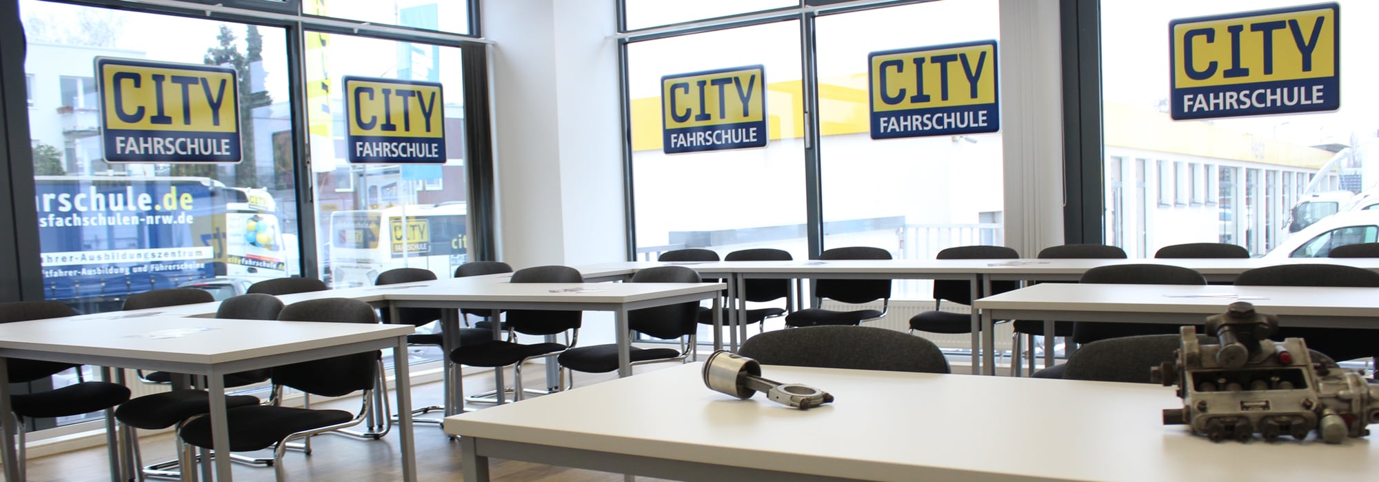 Es wird der Kursraum der Cityfahrschule gezeigt. Man sieht Tische und Stühle und an den Fenstern klebt das Logo der Cityfahrschule.