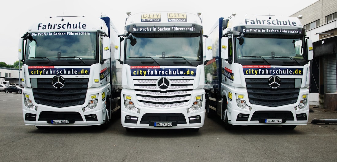 Drei LKW der Cityfahrschule stehen nebeneinander in einer Reihe. Die Fronten zeigen zur Kamera.