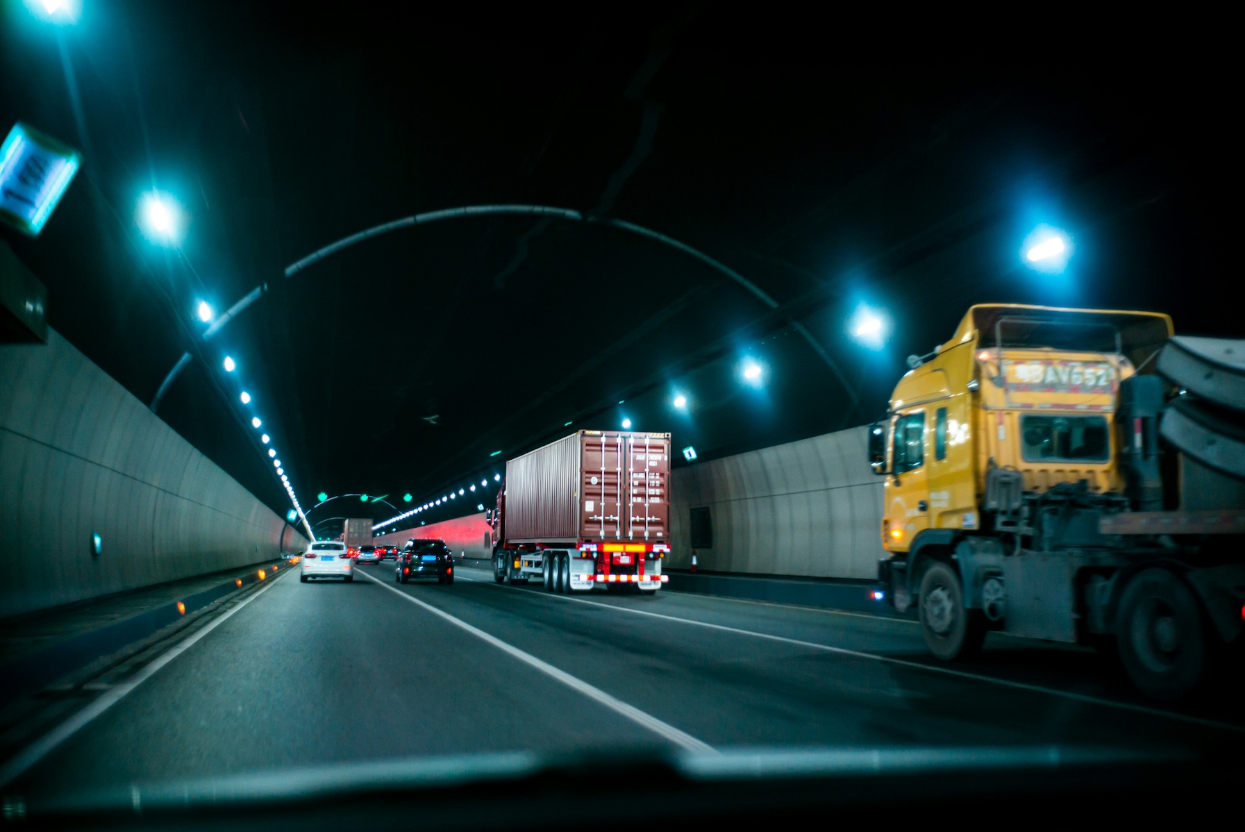 LKWs und Autos fahren durch einen beleuchteten, modernen Tunnel.