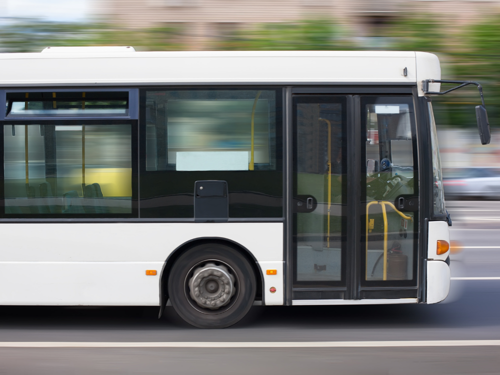 Hier sieht man einen weißen Bus, der auf der Straße fährt.